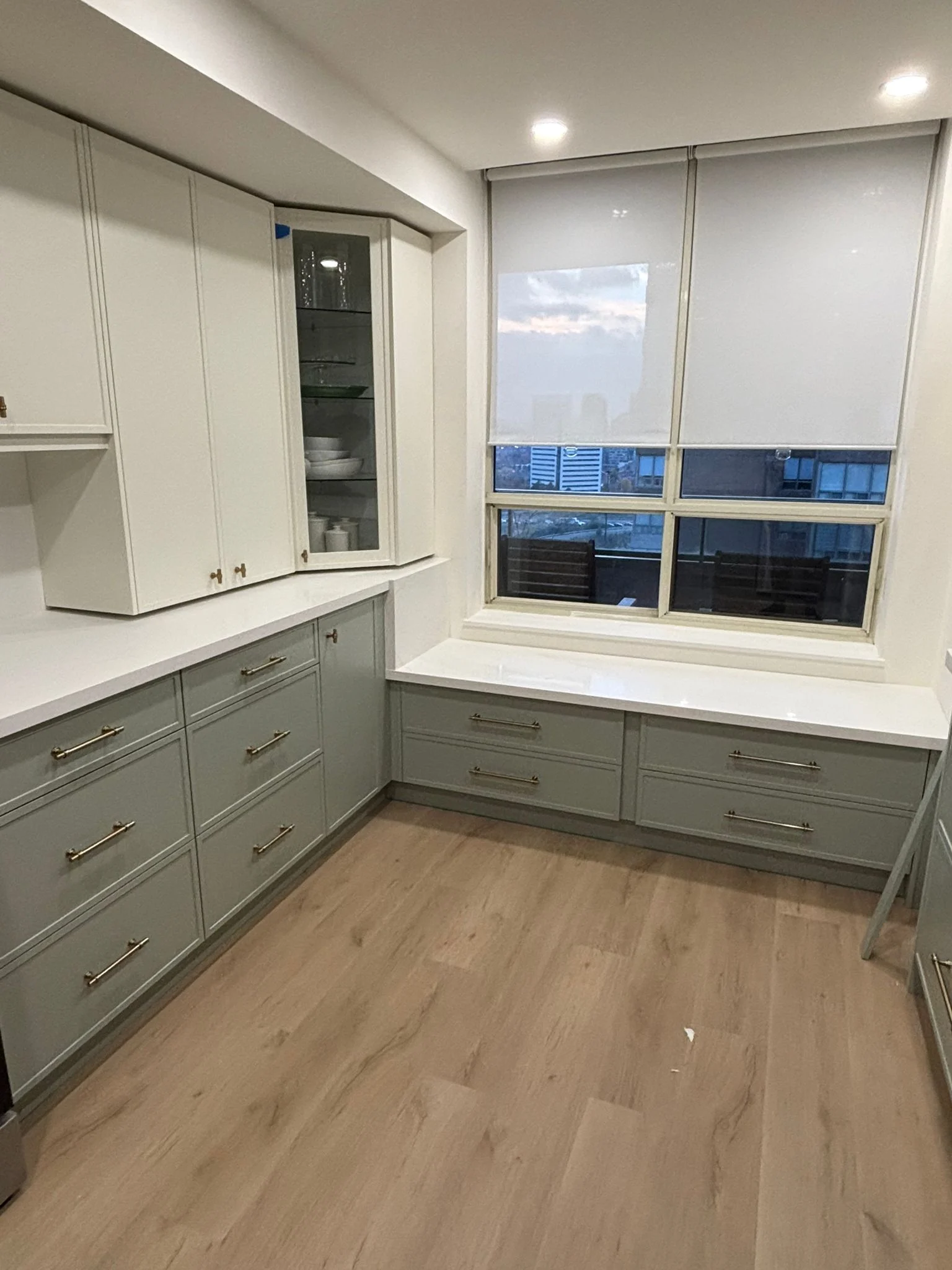 Sage green built-in cabinets with a window bench, white glass-front uppers and a city view
