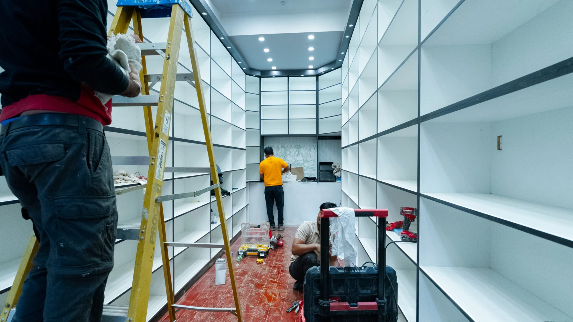 Tevola installers on ladders fitting floor to ceiling white shelving