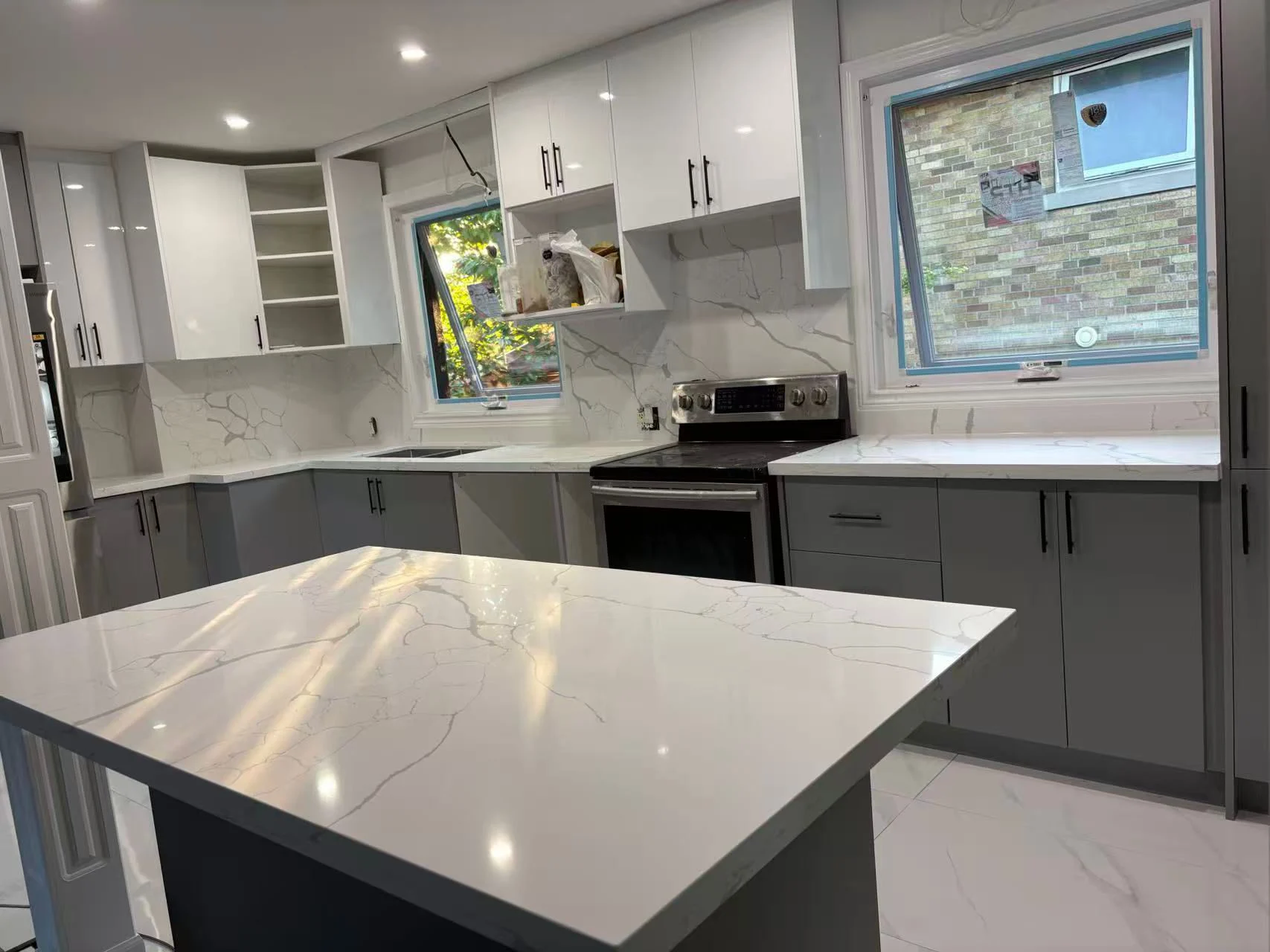 Kitchen with white upper cabinets, grey lowers, a quartz island and two windows