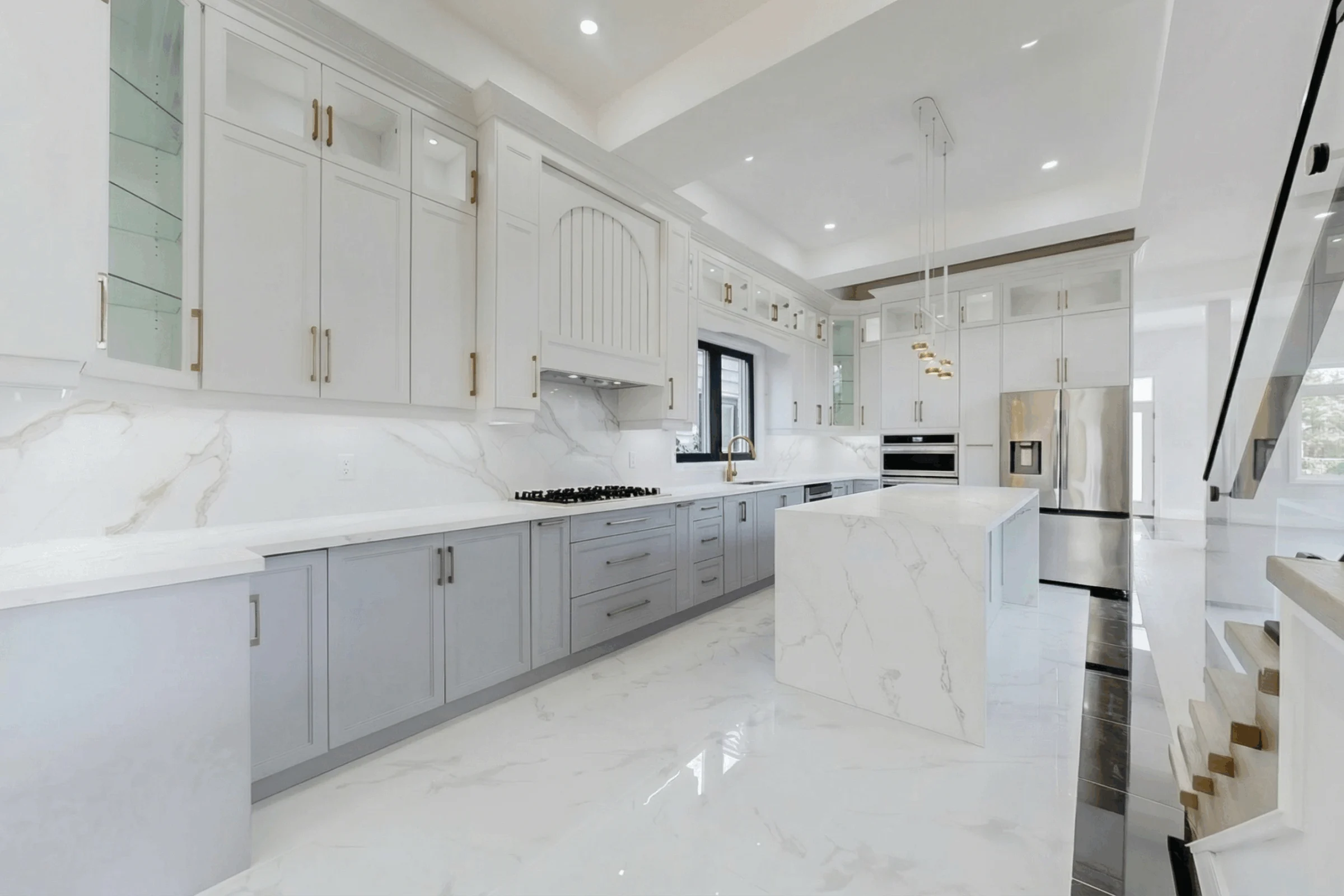 White custom kitchen with grey lower cabinets, a marble waterfall island and brass pendant lights