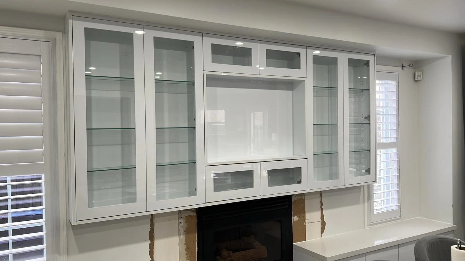 White built-in wall unit with glass-front cabinets framing a fireplace